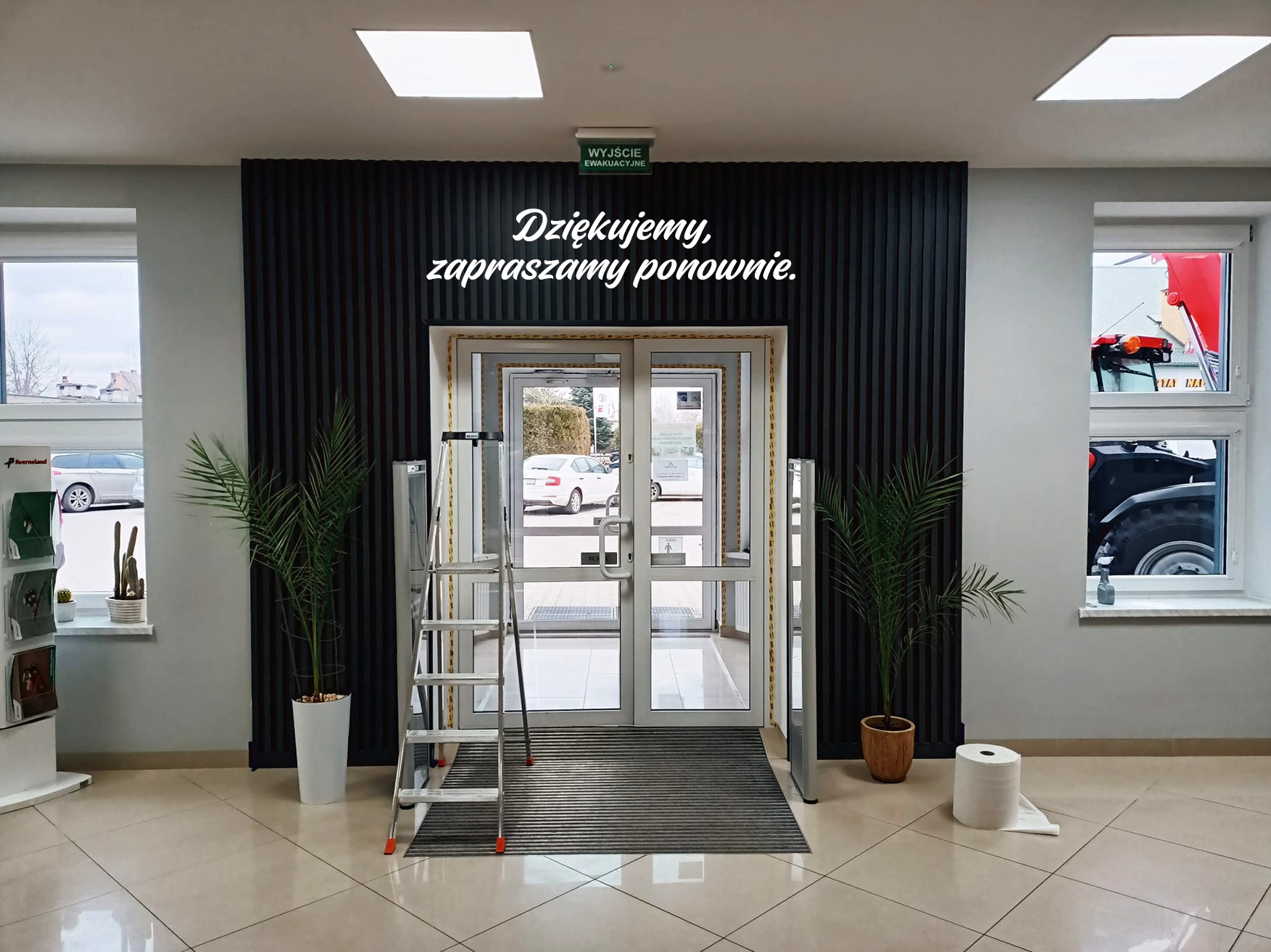 Wnętrze biura z napisem 'Dziękujemy, zapraszamy ponownie' nad wejściem, drabina oparta o futrynę, prawdopodobnie w trakcie montażu liter przestrzennych.