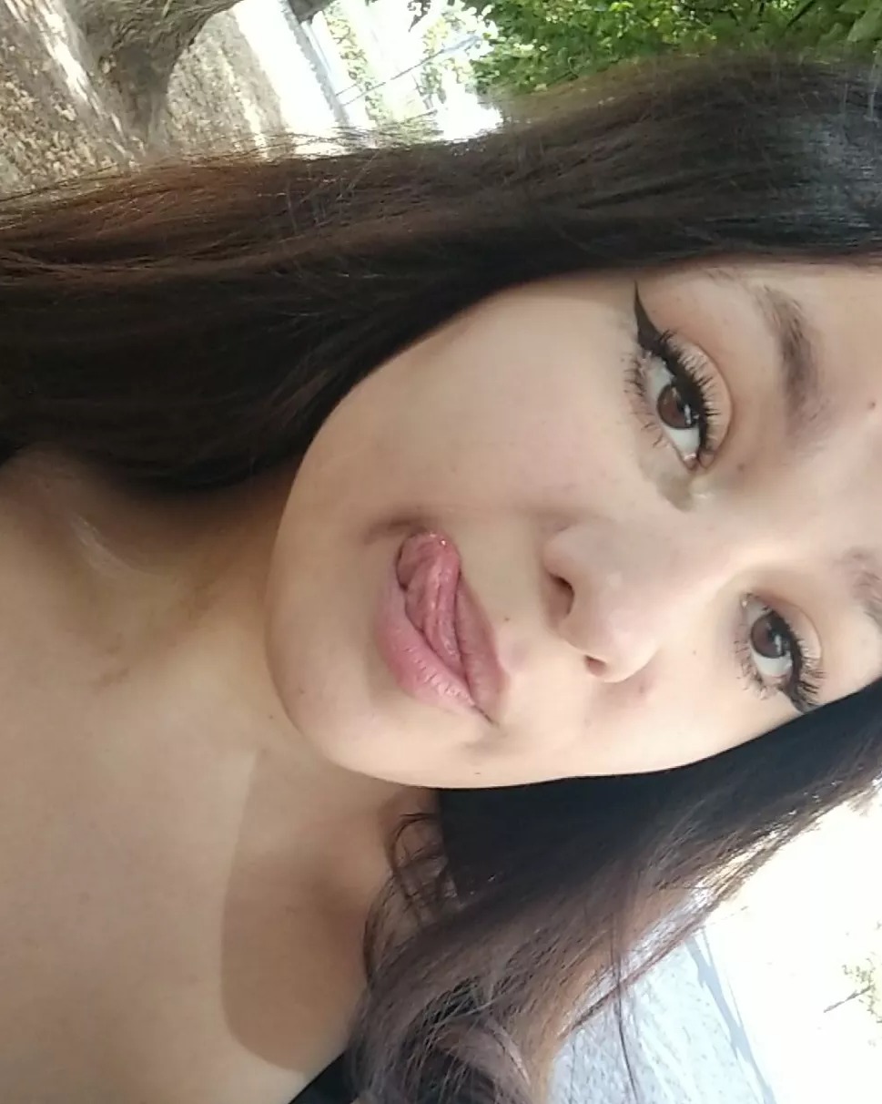 Portret młodej kobiety z długimi ciemnymi włosami, delikatnym makijażem oczu i wyciągniętym językiem, ujęcie z bliska.