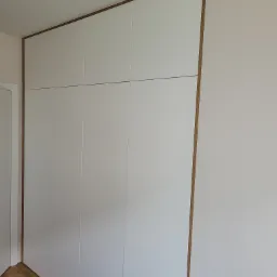 Biała szafa wnękowa z drewnianym obramowaniem, dopasowana do sufitu, zrealizowana w Pruszkowie.