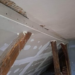 Krystian Drozdowski - Poddasze w trakcie prac: drewniane belki wspierają konstrukcję z płyty karton-gips, widoczne ślady szpachlowania i pianka montażowa w szczelinach.
