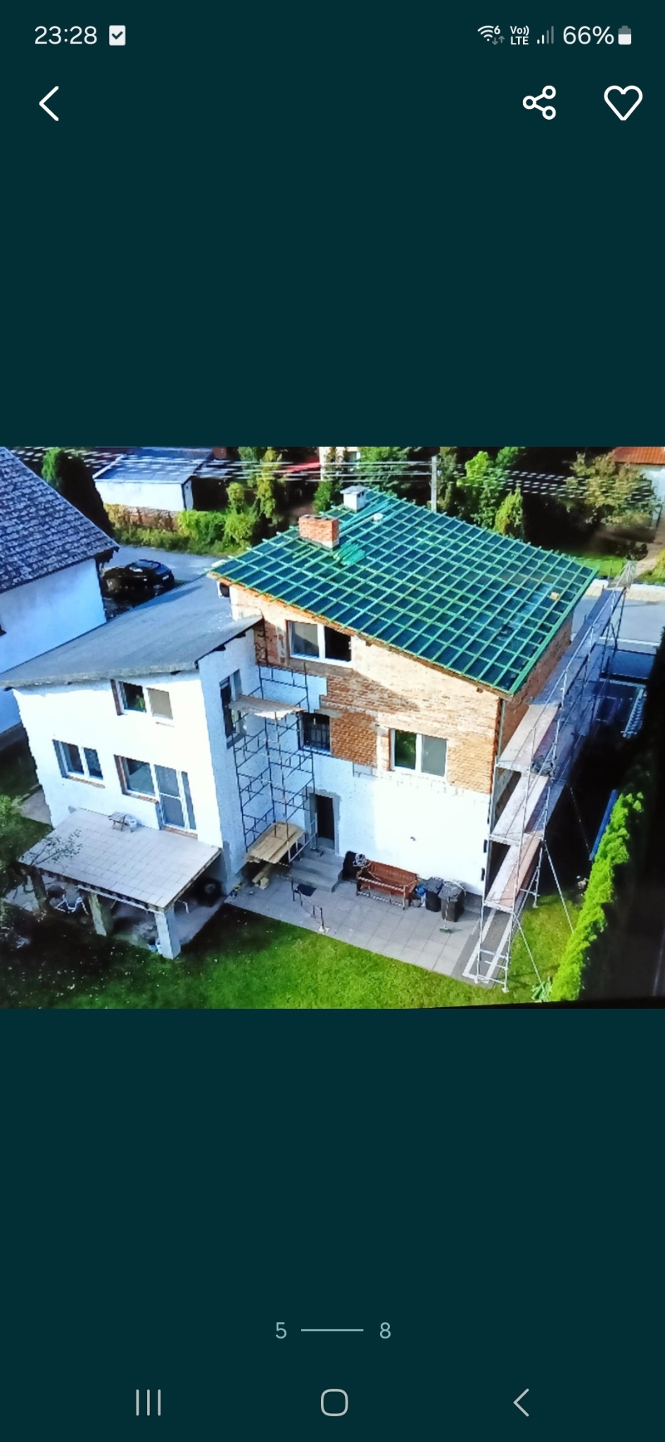 Dwupiętrowy dom w trakcie remontu elewacji i dachu, widoczne rusztowania i częściowo położona, zielona dachówka.