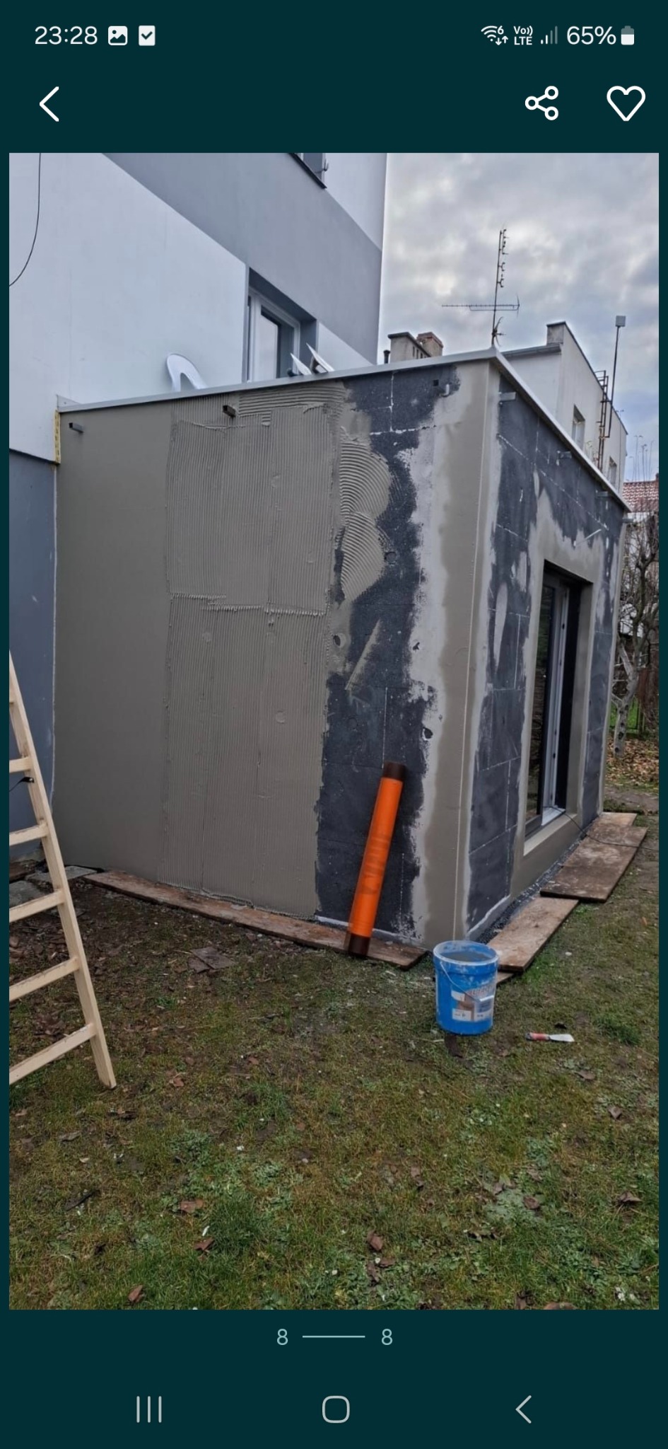 Ocieplanie elewacji budynku z widocznym styropianem i nałożoną warstwą kleju z charakterystycznymi rowkami, obok stoi niebieskie wiadro i pomarańczowa rolka, a w tle widać drabinkę.