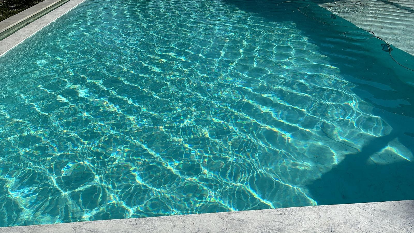 Turkusowa woda w basenie z marmurowym obramowaniem, widoczne refleksy słoneczne na dnie.