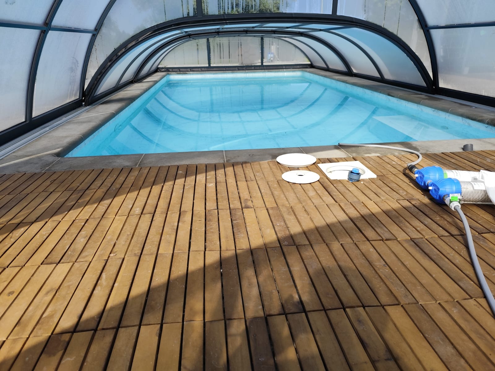 Zadaszony basen z drewnianym tarasem, widoczne akcesoria do filtracji wody i elementy instalacyjne.