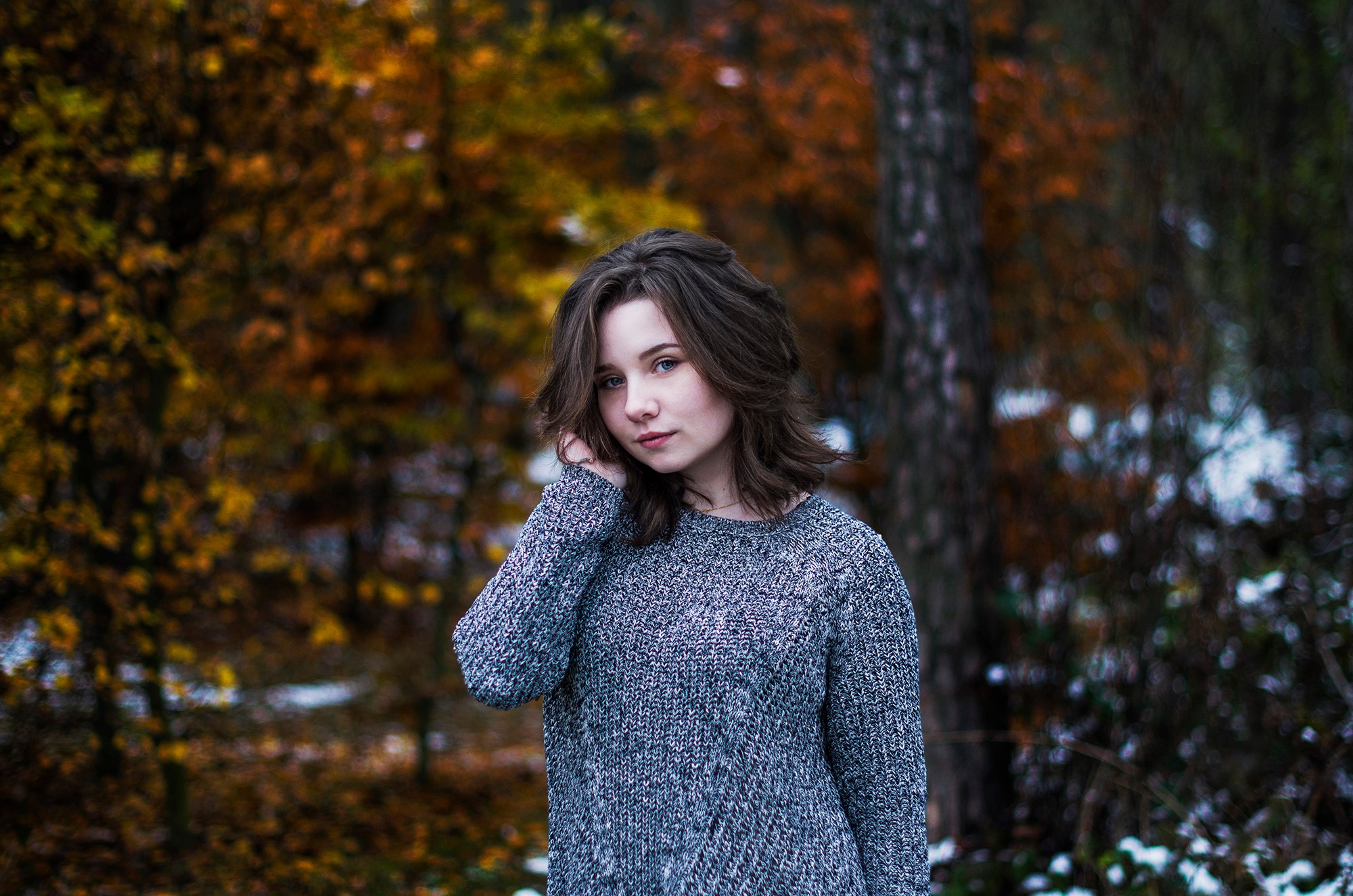 Portret młodej kobiety w szarym swetrze na tle jesiennego lasu z delikatnym efektem bokeh