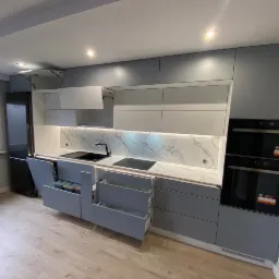 Nowoczesna, szara kuchnia z marmurowym panelem nad blatem, otwartymi szufladami z systemem sortowania odpadów i szufladami cargo, oświetleniem LED pod szafkami i w szufladach, oraz wbudowanym...