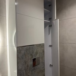 DiPol Meble - Dmytro Polishchuk - Biała szafka łazienkowa z otwartymi drzwiczkami, widoczne półki wewnątrz. Szafka zamontowana nad toaletą, z dekoracyjną płytką na ścianie. Minimalistyczny design.