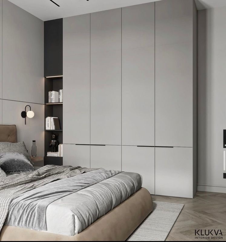 Nowoczesna sypialnia z szarą zabudową szaf wnękowych, czarnymi uchwytami i półką z podświetleniem, widoczna część łóżka z szarą pościelą i dywanem na parkiecie.