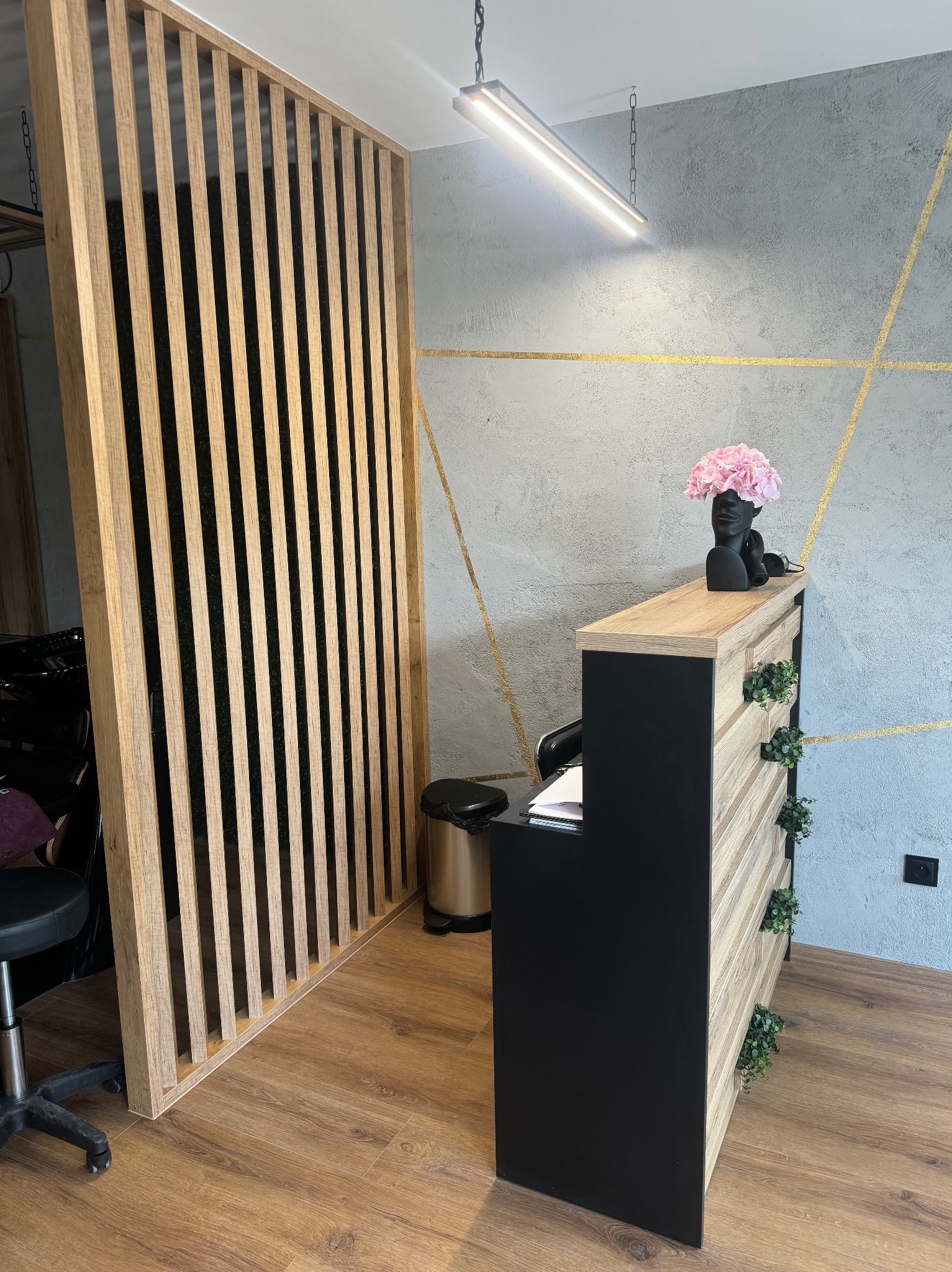 Drewniana ścianka działowa z pionowych listew i lada recepcyjna z roślinami w nowoczesnym salonie. Dekoracyjna ściana z geometrycznym wzorem w tle.