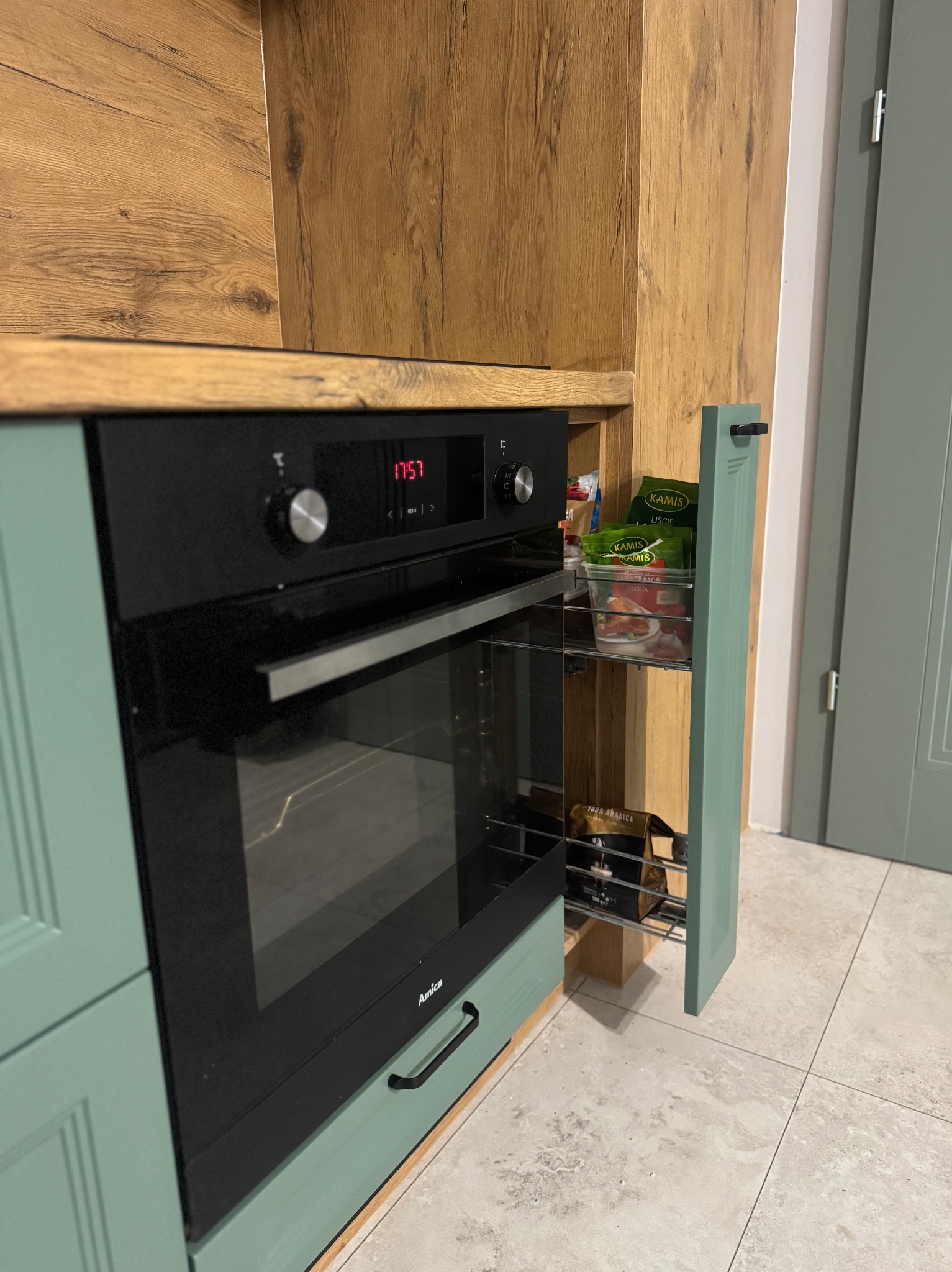 Nowoczesna kuchnia z zabudowaną piekarnikiem Amica i wysuwaną szafką cargo w kolorze miętowym, eksponująca detale wykończenia i funkcjonalne rozwiązania.
