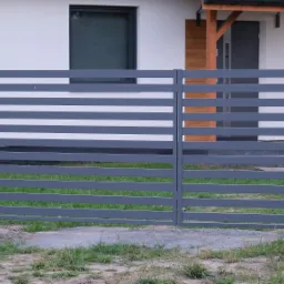Nowoczesne, poziome, szare przęsła ogrodzeniowe z metalu przed białym domem z szarymi oknami i drzwiami.