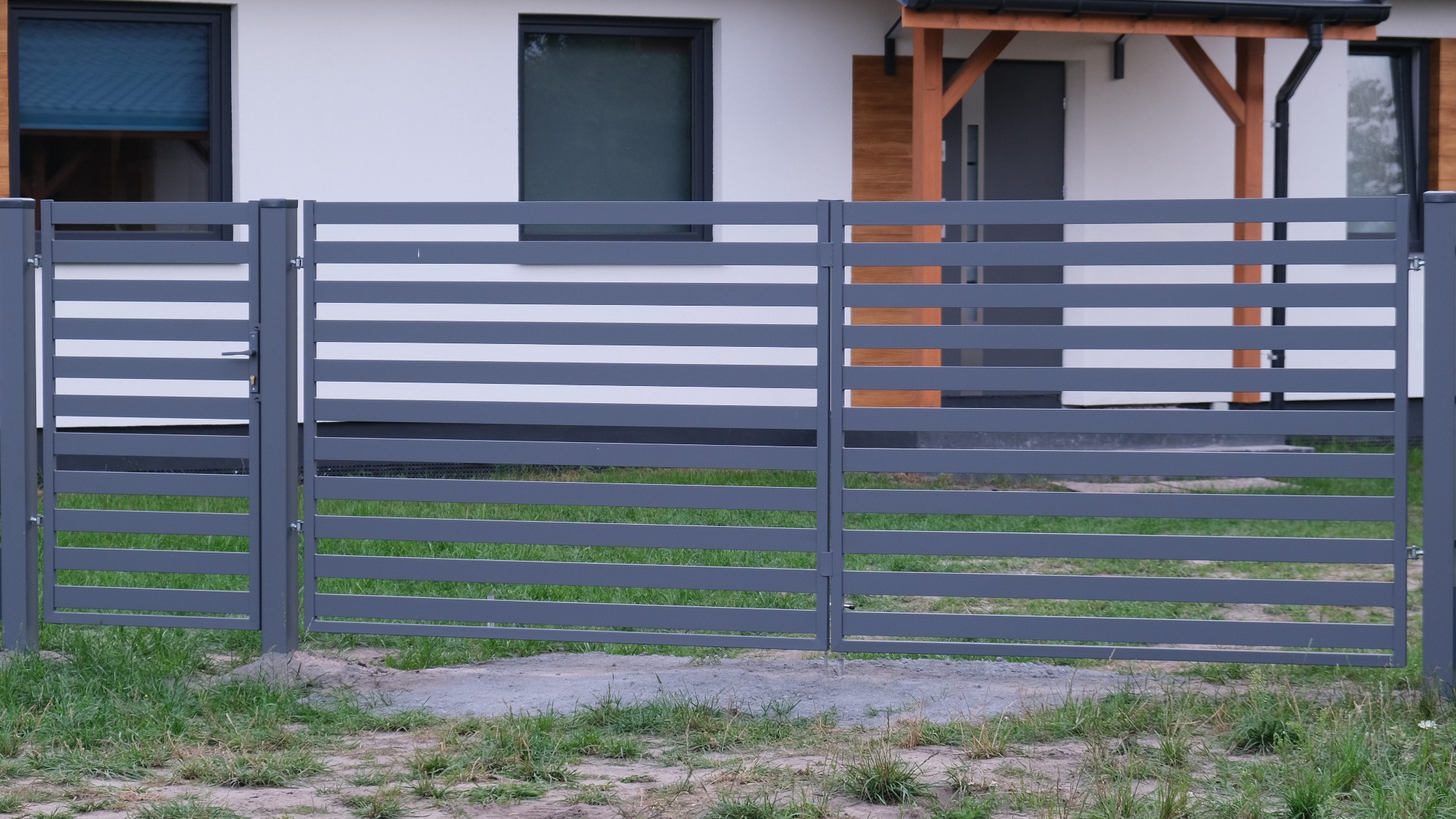 Nowoczesne, poziome, szare przęsła ogrodzeniowe z metalu przed białym domem z szarymi oknami i drzwiami.