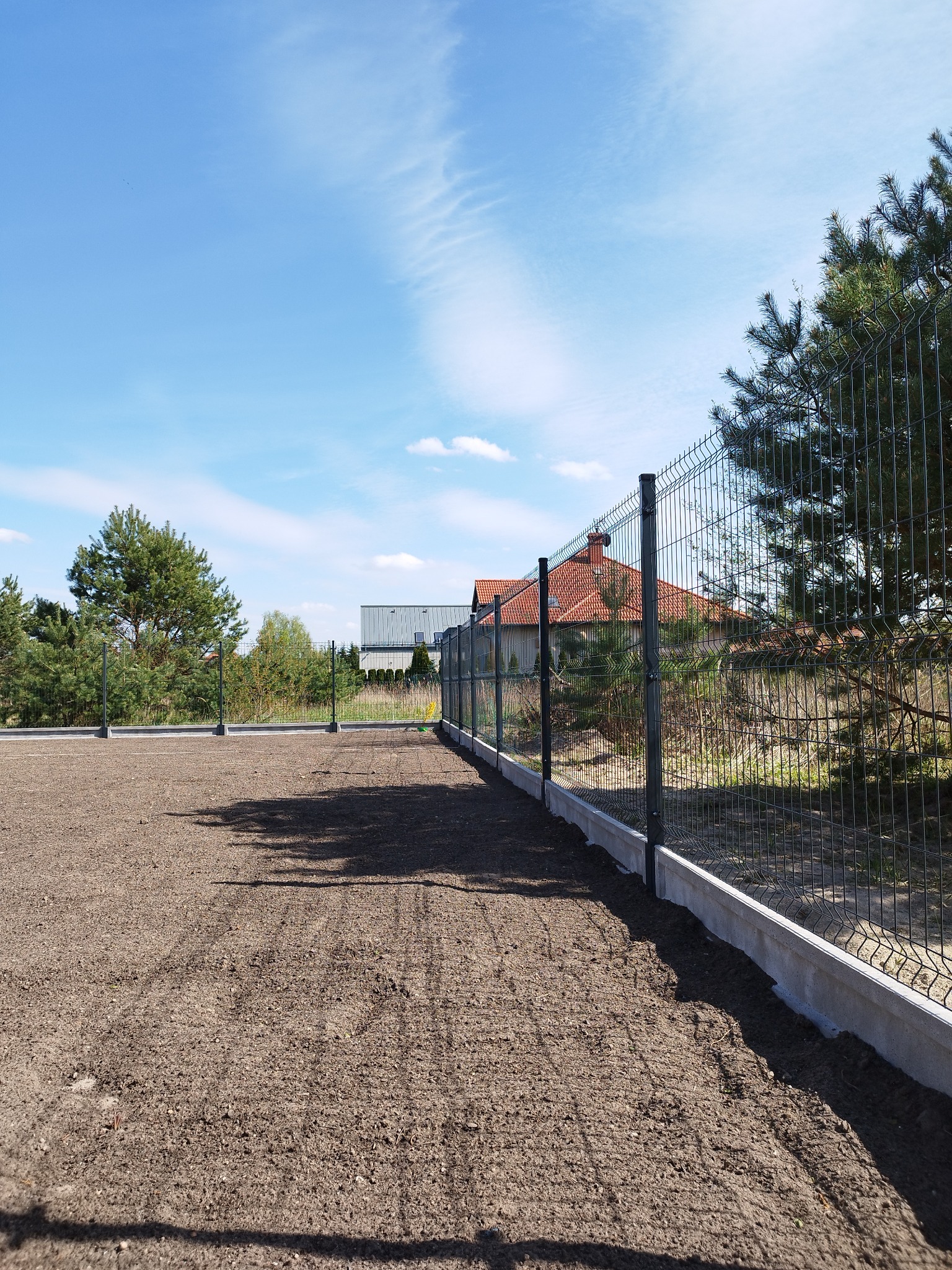 Nowoczesne ogrodzenie panelowe z podmurówką betonową, widok na przygotowany teren pod trawnik, słoneczny dzień.