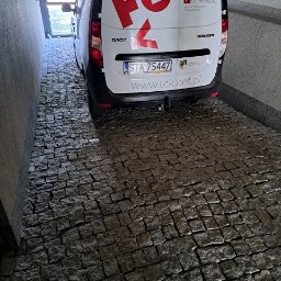 KKK Bruk - Dacia Dokker zaparkowana na wybrukowanym podjeździe z kostki granitowej, widok na tylną część pojazdu z logo firmy Tarnogórskie Centrum Kultury.