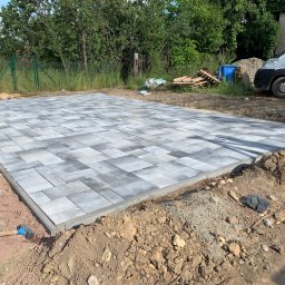 KKK Bruk - Ułożona szara kostka brukowa na przygotowanym podłożu, widoczny młotek brukarski, krawężniki i zaparkowany biały samochód dostawczy w tle.