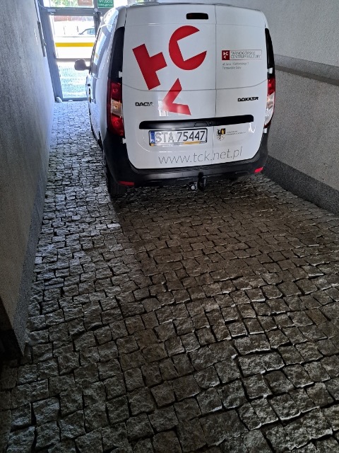 Dacia Dokker zaparkowana na wybrukowanym podjeździe z kostki granitowej, widok na tylną część pojazdu z logo firmy Tarnogórskie Centrum Kultury.