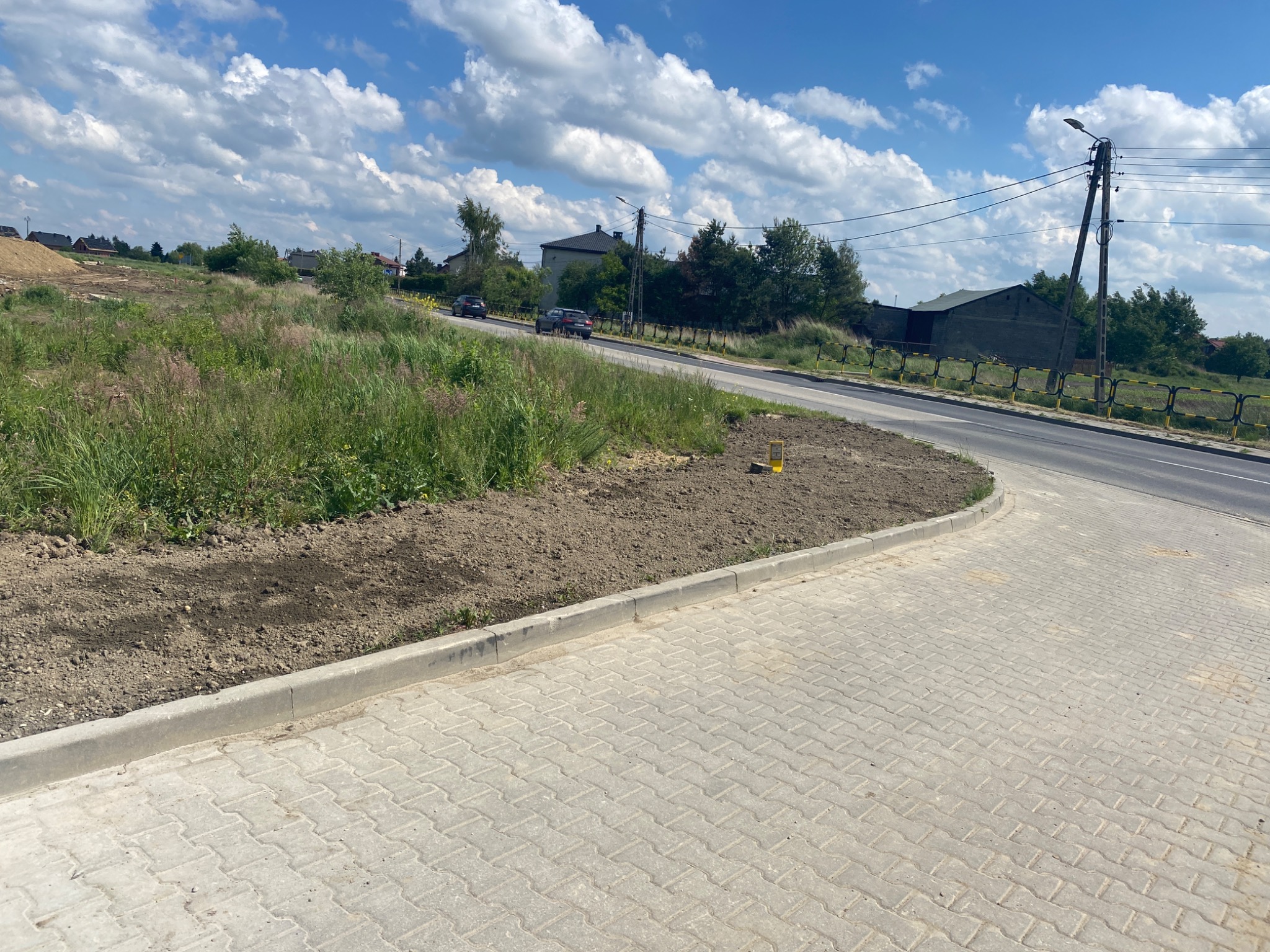 Nowo ułożona, jasnoszara kostka brukowa w Katowicach, z widocznym obrzeżem i przygotowanym terenem pod nasadzenia, w tle droga i zieleń.