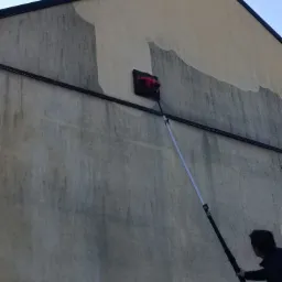 Czyszczenie elewacji budynku z użyciem szczotki na teleskopowym wysięgniku, widoczne różnice w kolorze elewacji przed i po czyszczeniu.