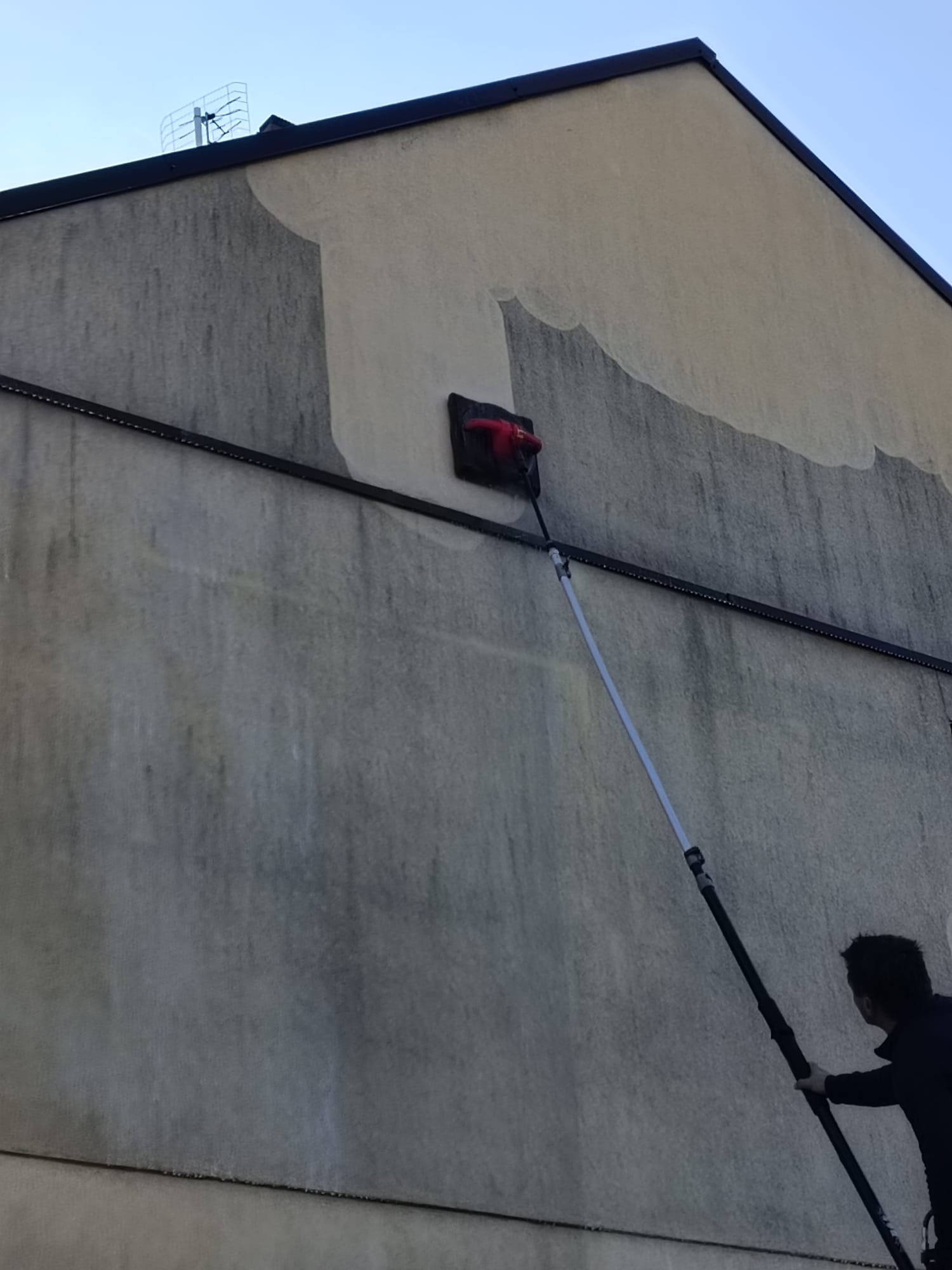 Czyszczenie elewacji budynku z użyciem szczotki na teleskopowym wysięgniku, widoczne różnice w kolorze elewacji przed i po czyszczeniu.