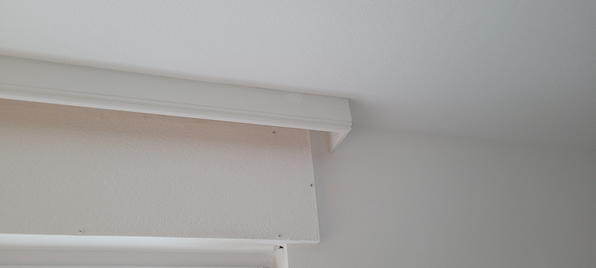 Fragment ściany z zamocowaną płytą kartonowo-gipsową, widoczne wkręty mocujące i biała listwa dekoracyjna pod sufitem.