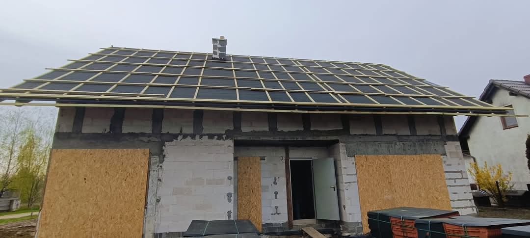 Budowa dachu: widok na budynek z zamontowaną membraną dachową i łatami, przygotowany do dalszego krycia, z widocznym kominem w trakcie obróbki.