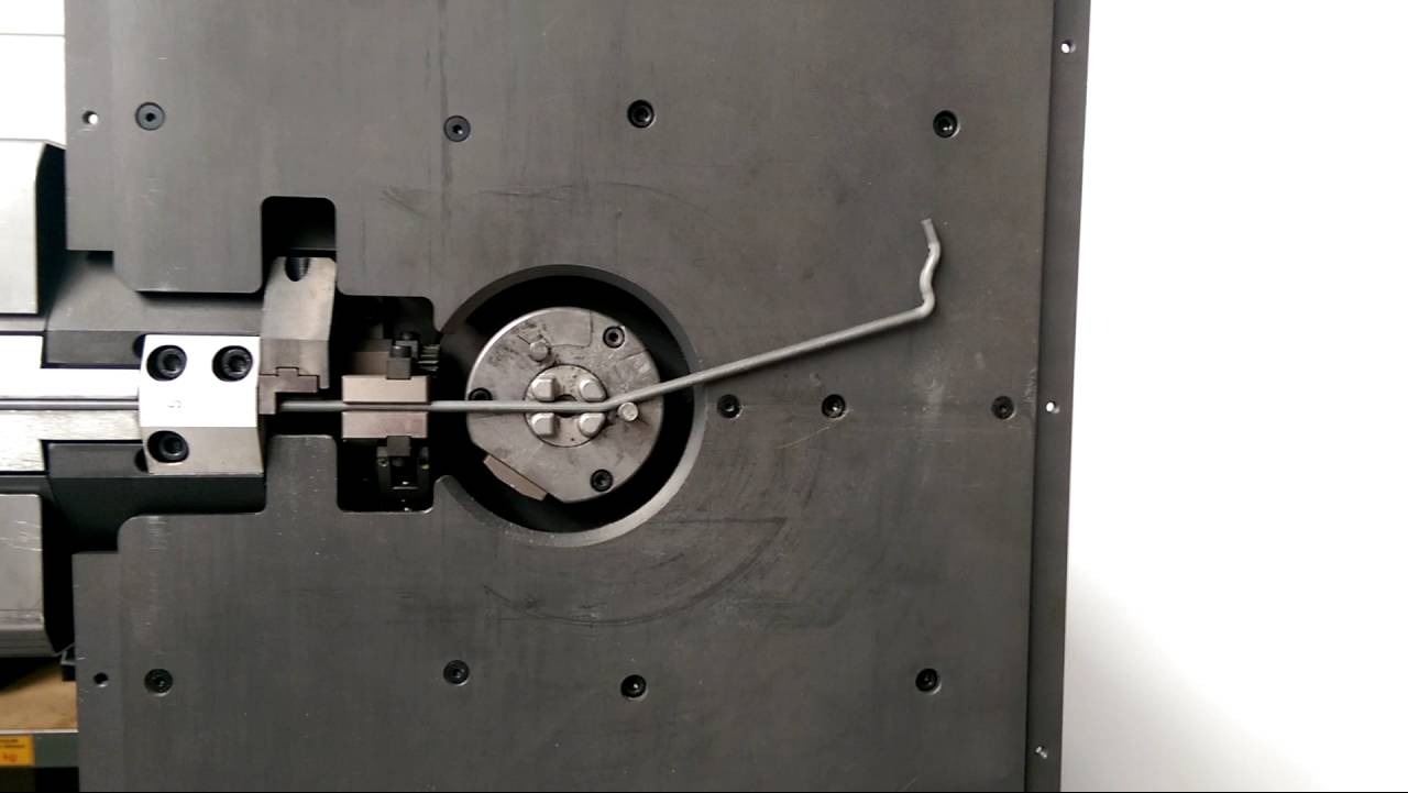 Proces gięcia pręta zbrojeniowego na maszynie CNC, widoczny mechanizm obrotowy i uformowany fragment pręta.