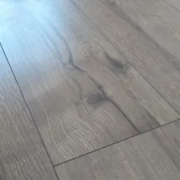 Ułożone panele podłogowe w odcieniach szarości, widoczne delikatne słoje drewna i subtelne refleksy światła.