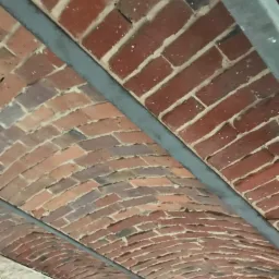 Ceglany łuk stropowy z widoczną metalową konstrukcją wsporczą w trakcie renowacji, z różnicami w odcieniach cegieł i fug.