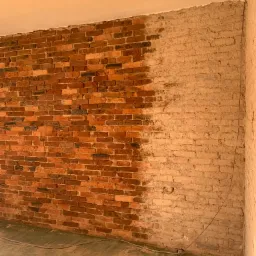 Częściowo odrestaurowana ceglana ściana wewnętrzna, z lewej strony cegła w naturalnym kolorze, z prawej oczyszczona i przygotowana do dalszych prac wykończeniowych.