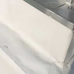 Szczegółowe ujęcie fragmentu dachu z białym pokryciem i metalową obróbką blacharską, widoczne łączenia i elementy mocujące.