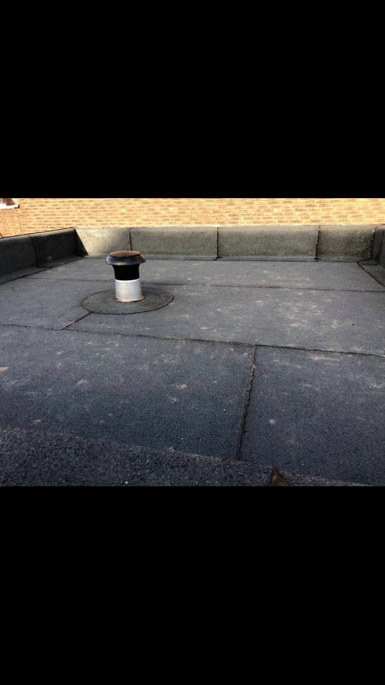 Płaski dach pokryty papą z kominkiem wentylacyjnym, widoczne łączenia papy i obróbki blacharskie przy krawędzi dachu.