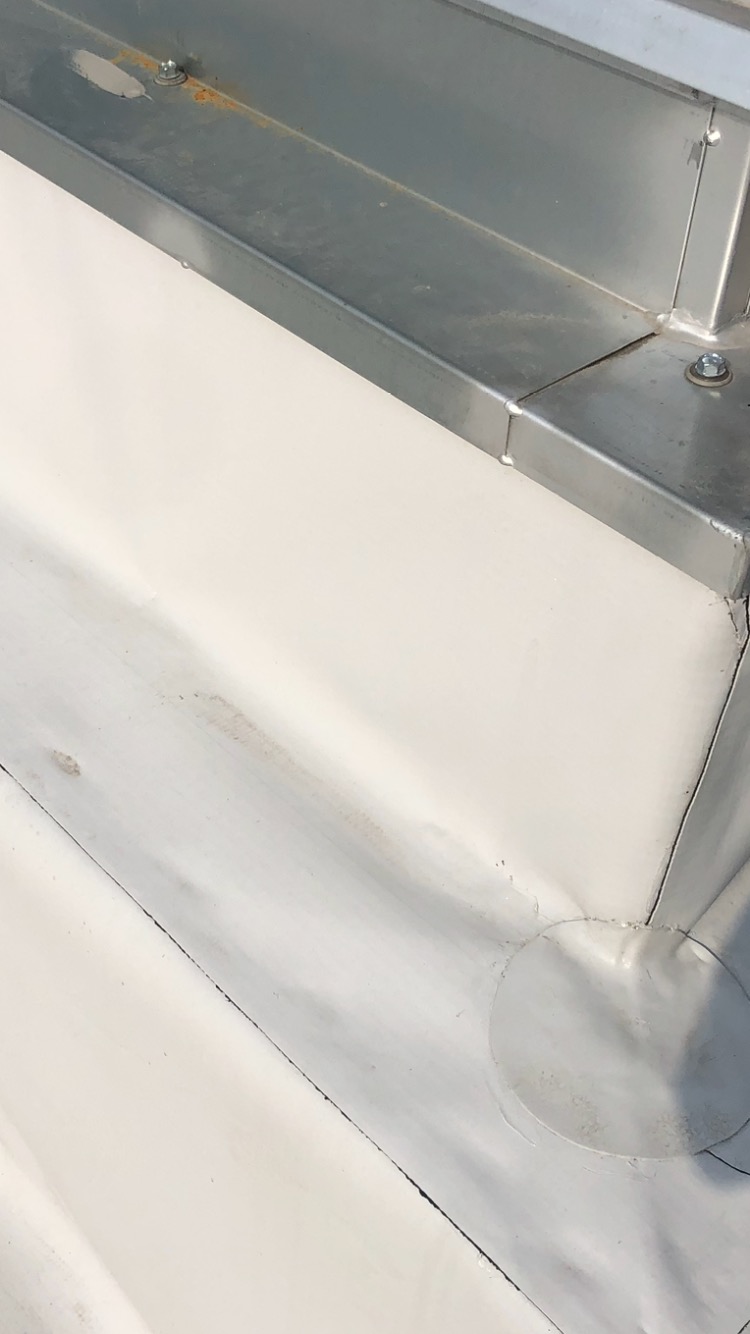 Szczegółowe ujęcie fragmentu dachu z białym pokryciem i metalową obróbką blacharską, widoczne łączenia i elementy mocujące.