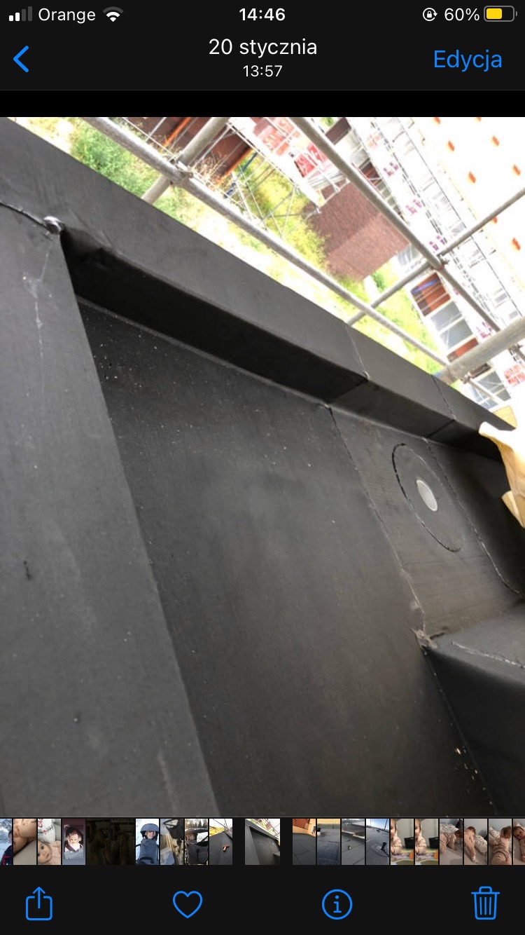 Fragment płaskiego dachu pokrytego czarną papą termozgrzewalną z widocznym kominkiem odpowietrzającym w Oświęcimiu, w tle rusztowanie i budynki.