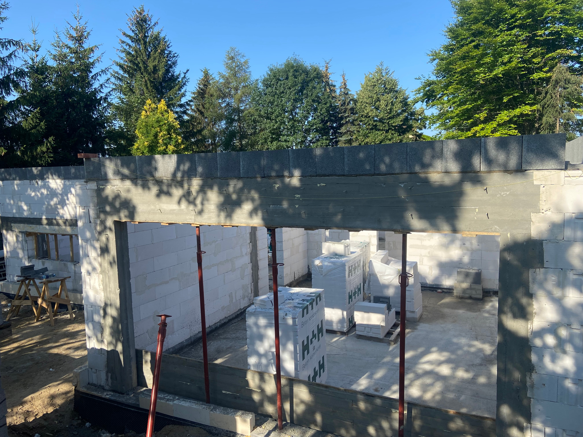 Budowa domu z betonu komórkowego w Poznaniu: wznoszenie ścian z bloczków H+H, widoczne podpory szalunkowe i palety z materiałem.