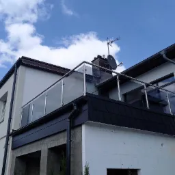 Zewnętrzna balustrada ze szkła hartowanego i stali nierdzewnej na balkonie budynku, widoczna antena satelitarna na dachu.