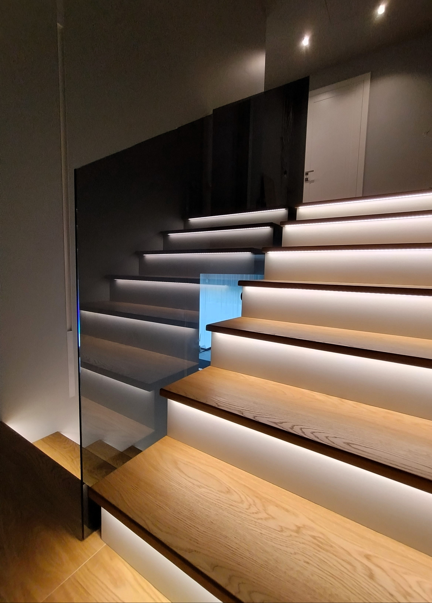 Nowoczesne, drewniane schody z podświetleniem LED i szklaną barierką, widok z dołu, minimalistyczny design.