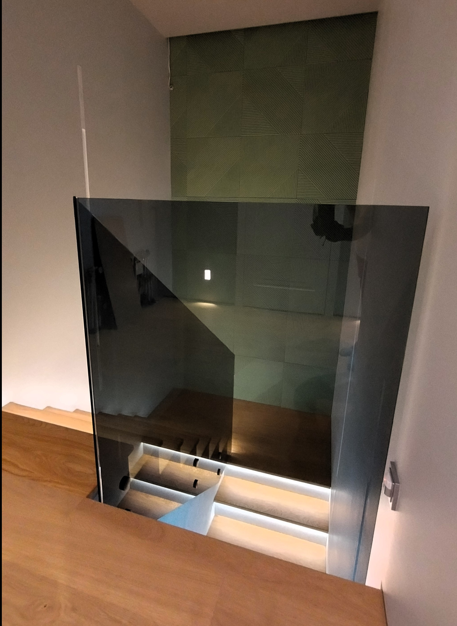 Szklana balustrada zabezpieczająca schody z podświetleniem LED, widok z góry na drewniane stopnie i minimalistyczny design.