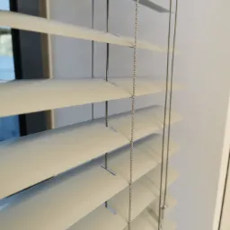 Jasne, aluminiowe listwy żaluzji w oknie, widoczne sznurki regulacyjne, Wrocław.