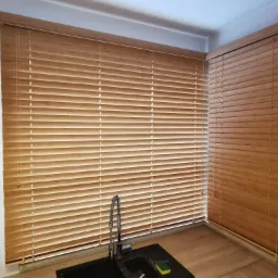 Zamknięte żaluzje drewniane w kuchni z widocznym kranem i zlewem, ciepłe oświetlenie.