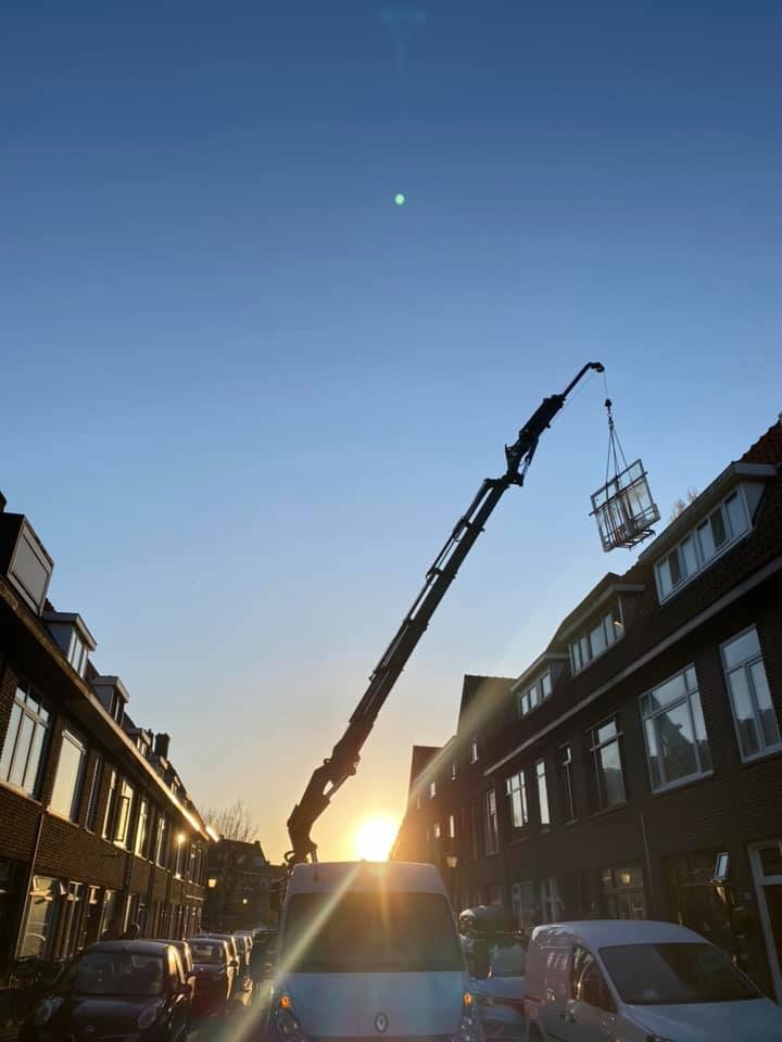 Montaż okna za pomocą dźwigu na tle zachodzącego słońca w zabudowie miejskiej.