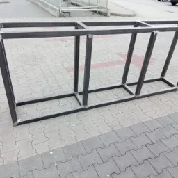 Spawana, surowa konstrukcja regału z profili metalowych, widoczne spawy, ułożona na kostce brukowej.