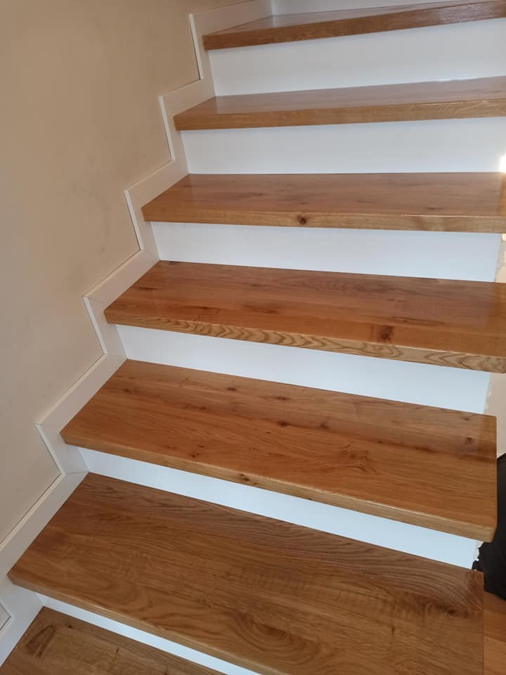 Jasne, dębowe stopnie schodów z białymi podstopnicami i listwami wykończeniowymi, widok z dołu, naturalne oświetlenie.