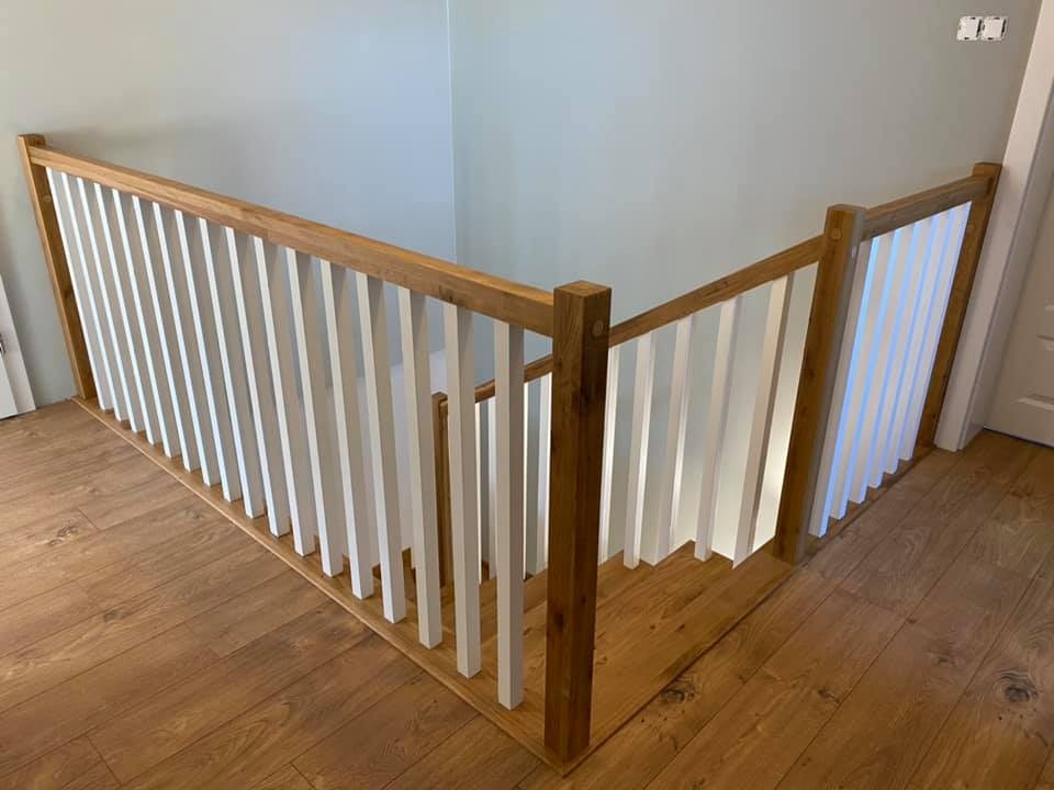 Jasne, nowoczesne balustrady z drewna i białych tralek, widoczne z góry na tle drewnianej podłogi i jasnych ścian.