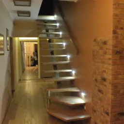 Nowoczesne schody drewniane z podświetleniem LED na każdym stopniu, prowadzące na wyższą kondygnację, obok ściana wykończona cegłą, widok z dołu.