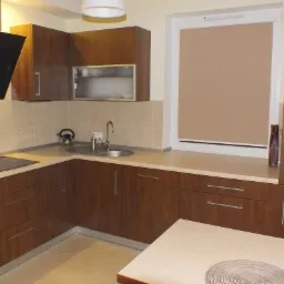 Nowoczesna kuchnia z brązowymi szafkami, beżowymi płytkami i blatem, czarnym okapem oraz okrągłym zlewem, uzupełniona o stół z podkładkami w odcieniach brązu.