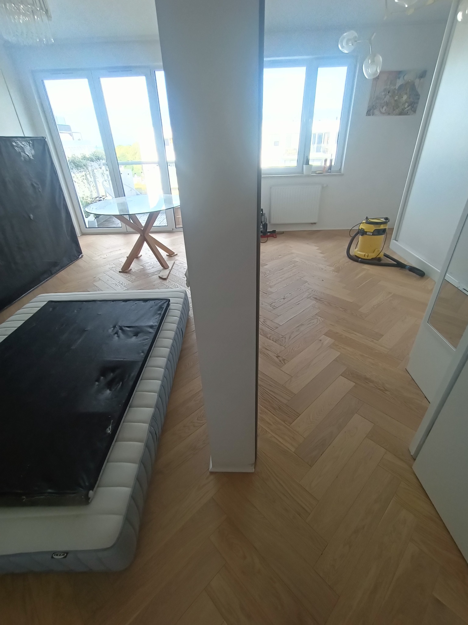 Ułożony parkiet w jodełkę francuską, zabezpieczony folią, z widocznym odkurzaczem przemysłowym i pozostałościami po remoncie w jasnym pomieszczeniu.