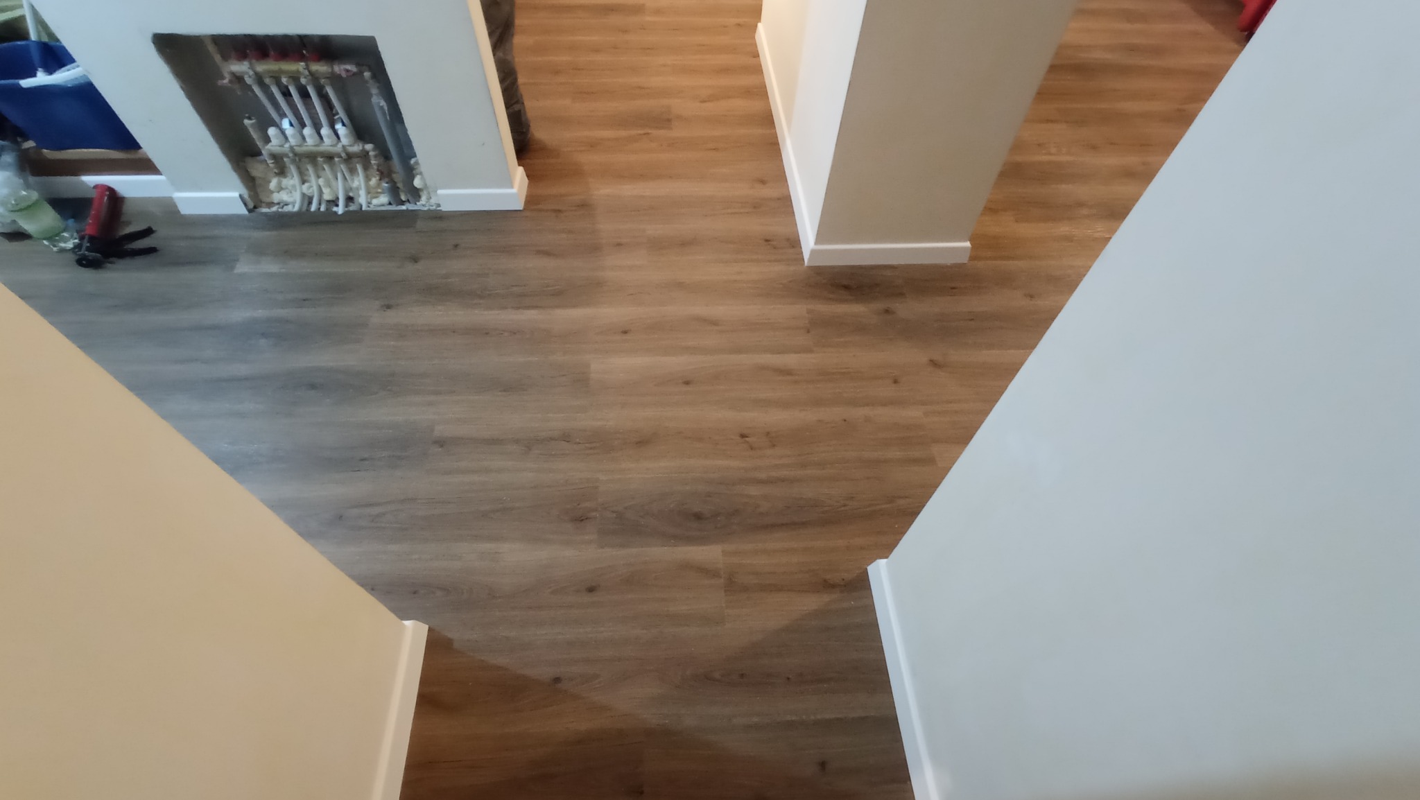 Ułożona podłoga panelowa w odcieniach brązu, widoczne białe listwy przypodłogowe i fragment instalacji grzewczej w ścianie przed zabudową.