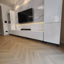 Piotr Kaczor-Usługi Remontowo Budowlane - Nowoczesny salon z białymi meblami na tle marmurowej ściany i parkietem ułożonym w jodełkę. Podświetlenie LED dodaje elegancji. Minimalistyczny design.