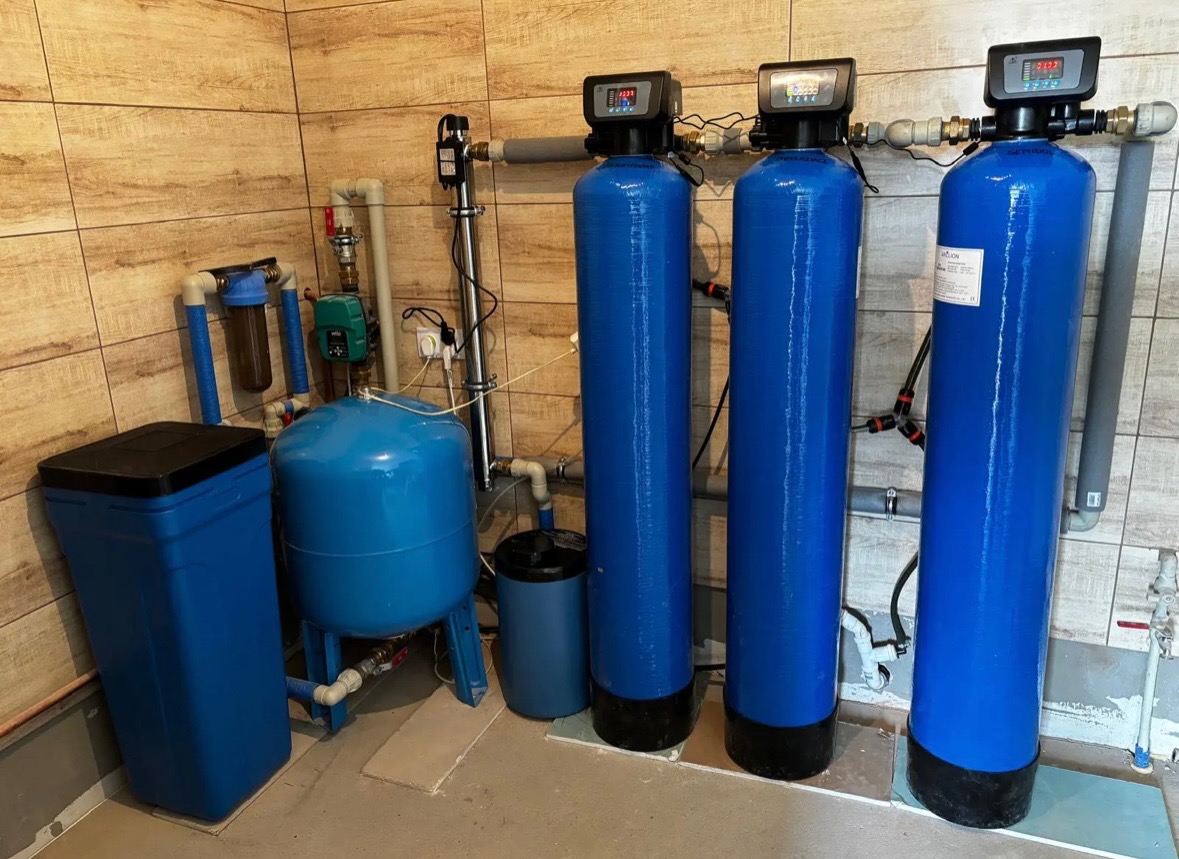 Kompletna instalacja uzdatniania wody w Kożuchowie, z trzema pionowymi zbiornikami filtracyjnymi z wyświetlaczami, zbiornikiem hydroforowym i pojemnikiem na sól, umieszczona w pomieszczeniu...