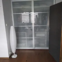 Wnętrze pokoju z przesuwną szafą z mlecznego szkła, widoczna podłoga z paneli, lampa podłogowa w kształcie kokonu i element dekoracyjny na ścianie.